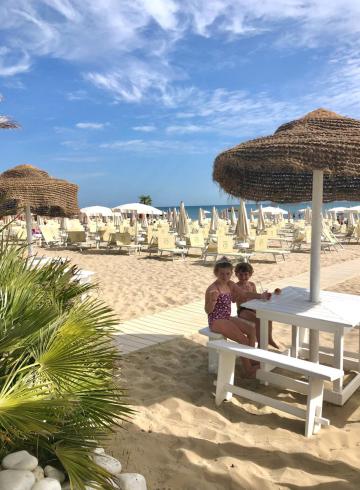 Sonniger Strand mit Kindern an einem Tisch unter Sonnenschirmen.