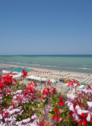 Strand mit bunten Sonnenschirmen und roten Blumen im Vordergrund.