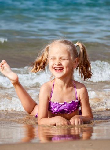 Smiling girl plays on the beach with waves.