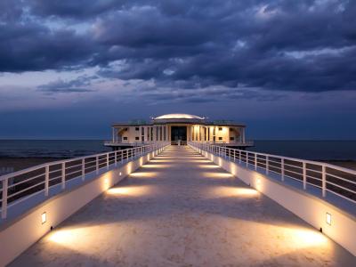 Seaside building with illuminated walkway at sunset.