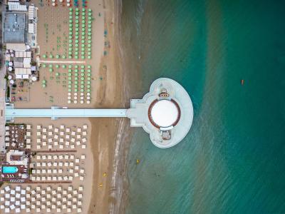 Veduta aerea di una spiaggia con ombrelloni e un molo sul mare.