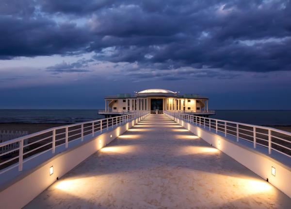 Seaside building with illuminated walkway at sunset.