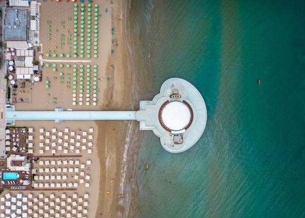 Veduta aerea di una spiaggia con ombrelloni e un molo sul mare.