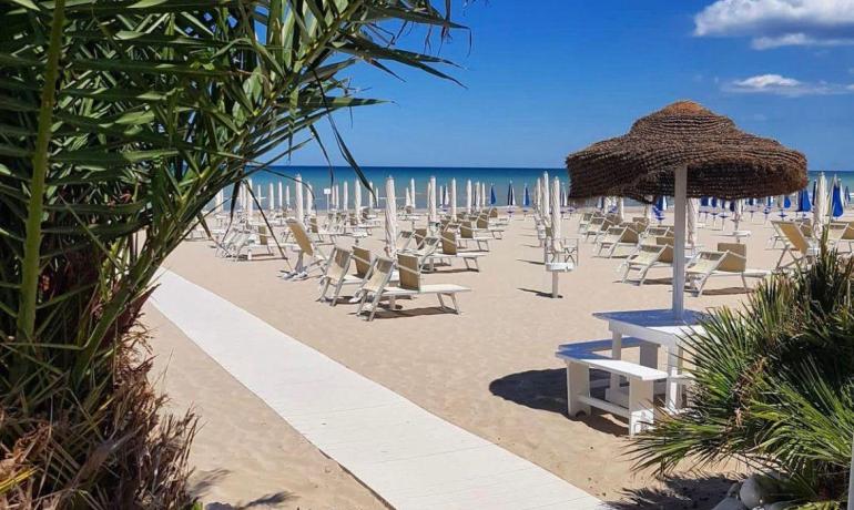 Sandy beach with umbrellas and palms under a blue sky.