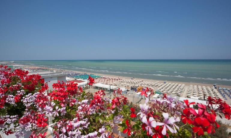 Spiaggia con ombrelloni colorati e fiori rossi in primo piano.