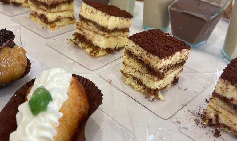 Varietà di dolci tra cui tiramisù e babà con panna.