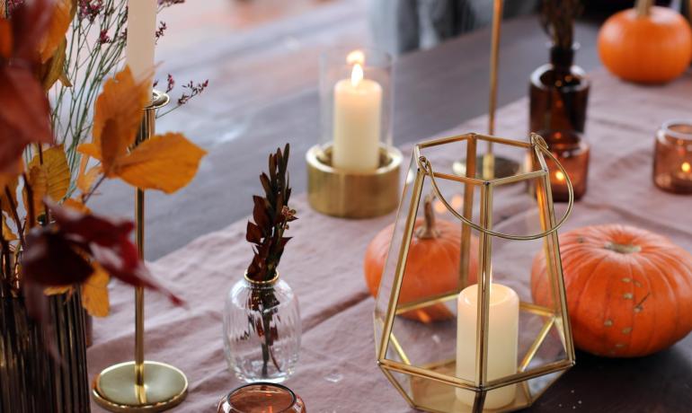 Autumn decor with candles, pumpkins, and colorful leaves on table.