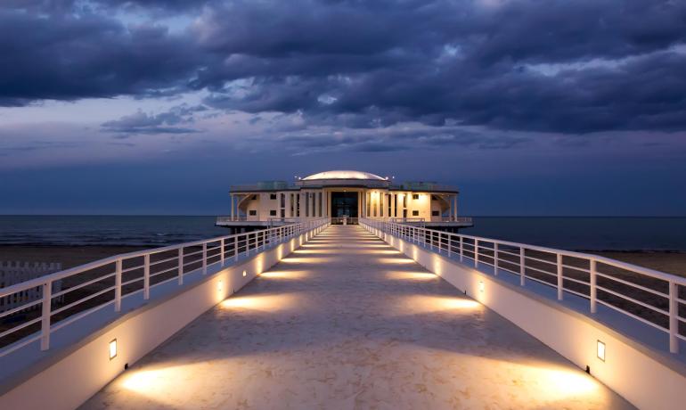 Bâtiment en bord de mer avec passerelle éclairée au coucher du soleil.