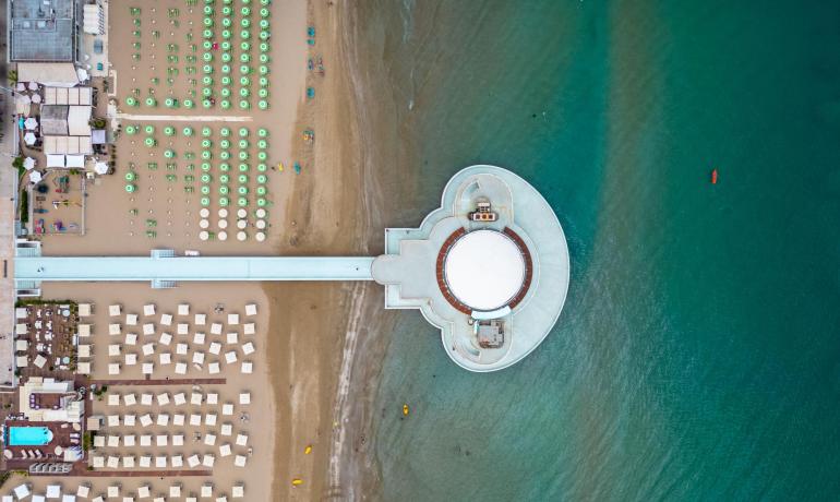 Luftaufnahme eines Strandes mit Sonnenschirmen und einem Pier über dem Meer.