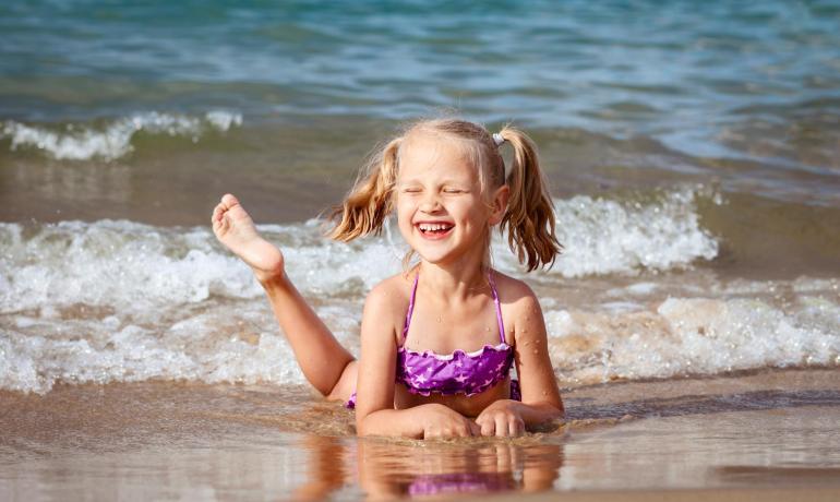 Smiling girl plays on the beach with waves.