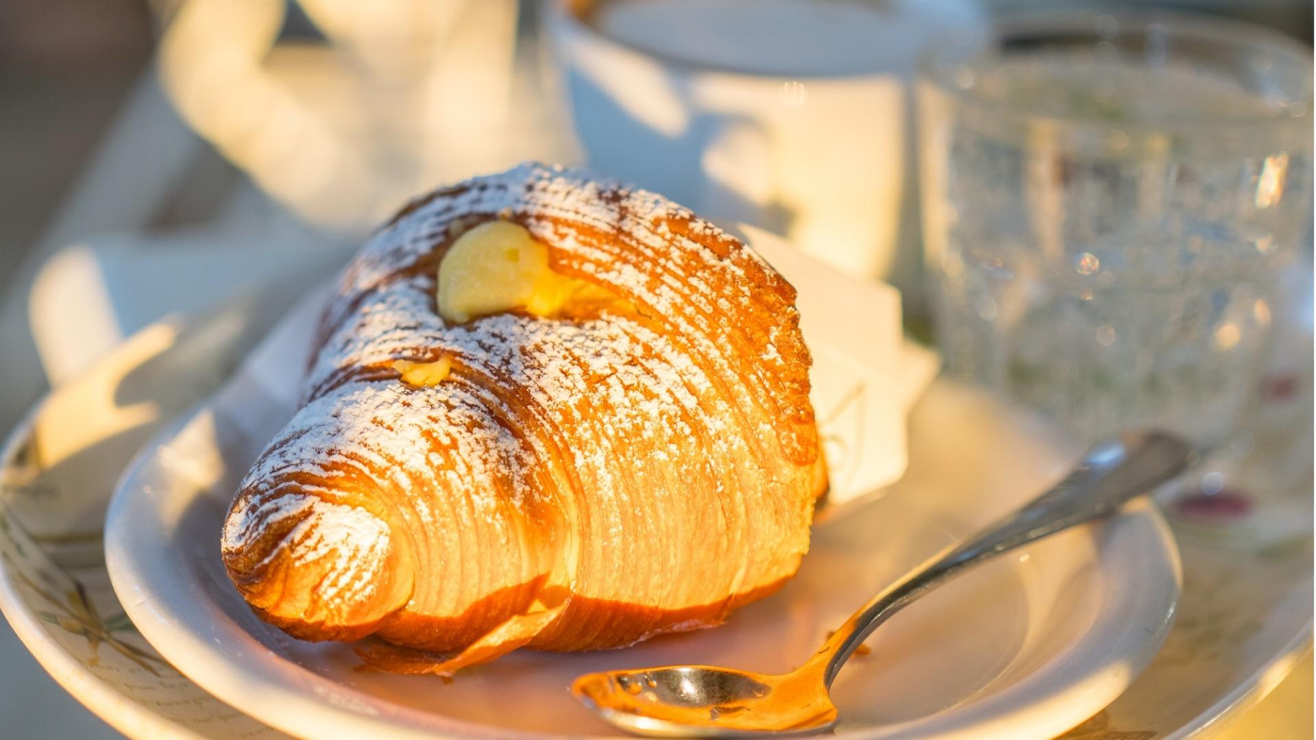 Cornetto alla crema spolverato di zucchero a velo su un piatto con cucchiaino.