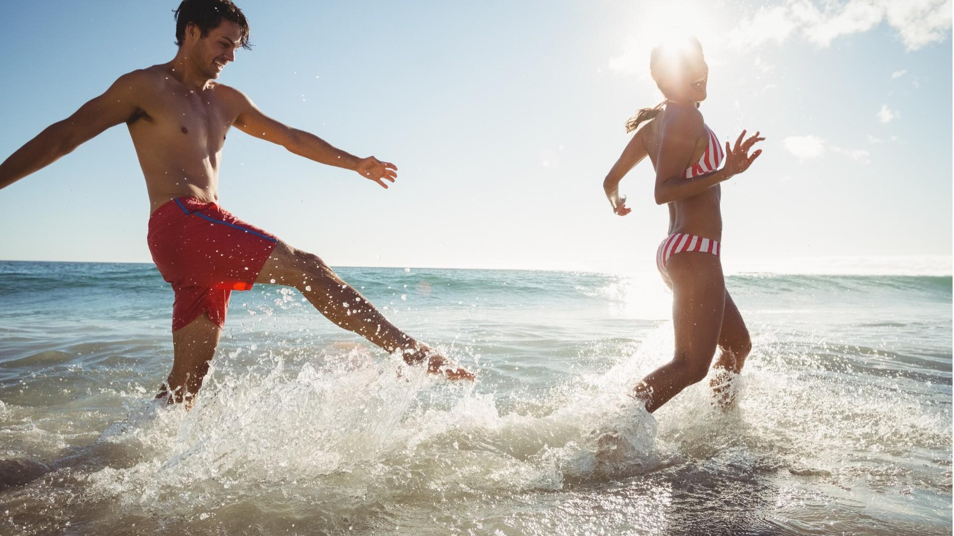 Due persone giocano felici in acqua al mare sotto il sole.