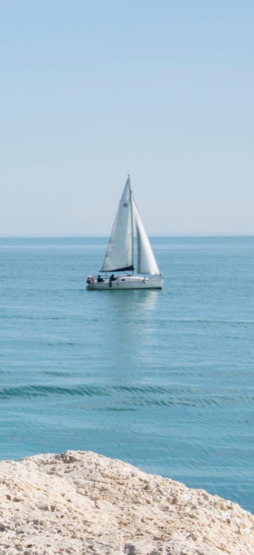 Barca a vela naviga su mare calmo con cielo sereno.